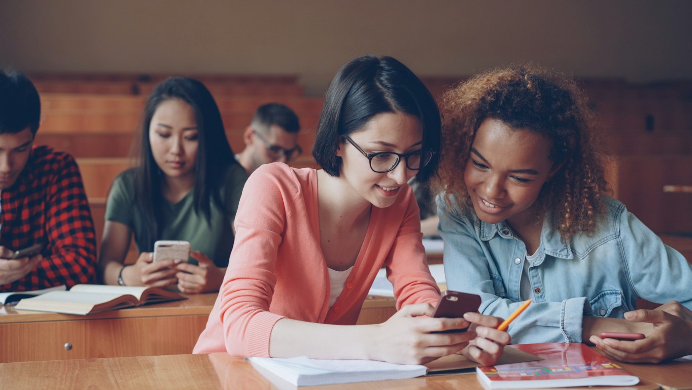 Estudiantes repasando con el celular en una biblioteca